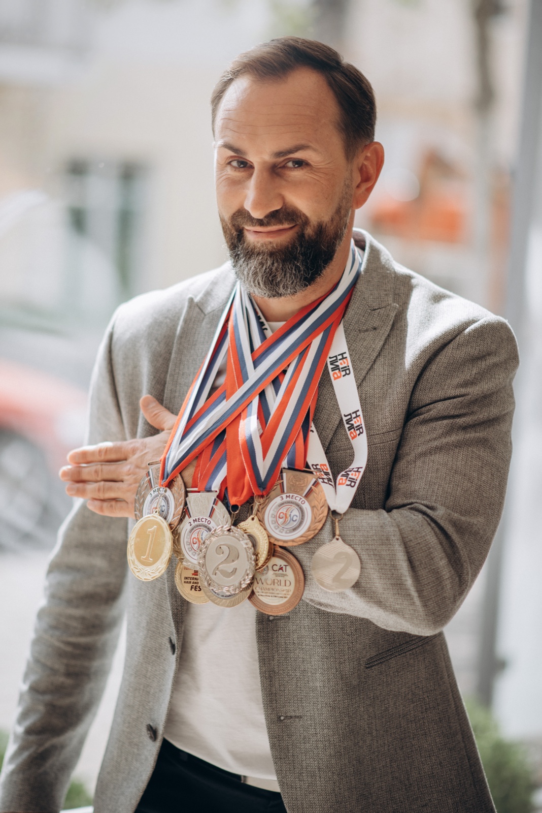 Dmitri Slabowski souriant, en veste gris clair, les médailles de ses concours autour du cou